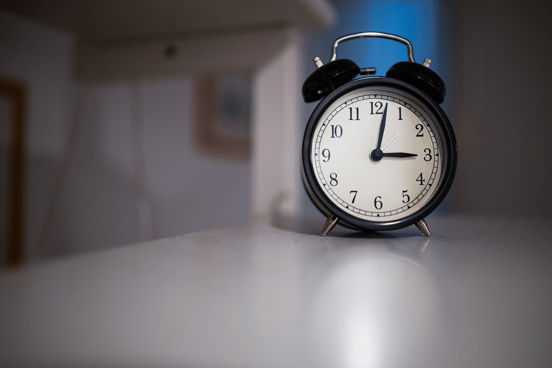 An alarm clock glowing 3 a.m. sits on a bedside table in a dark, quiet room.